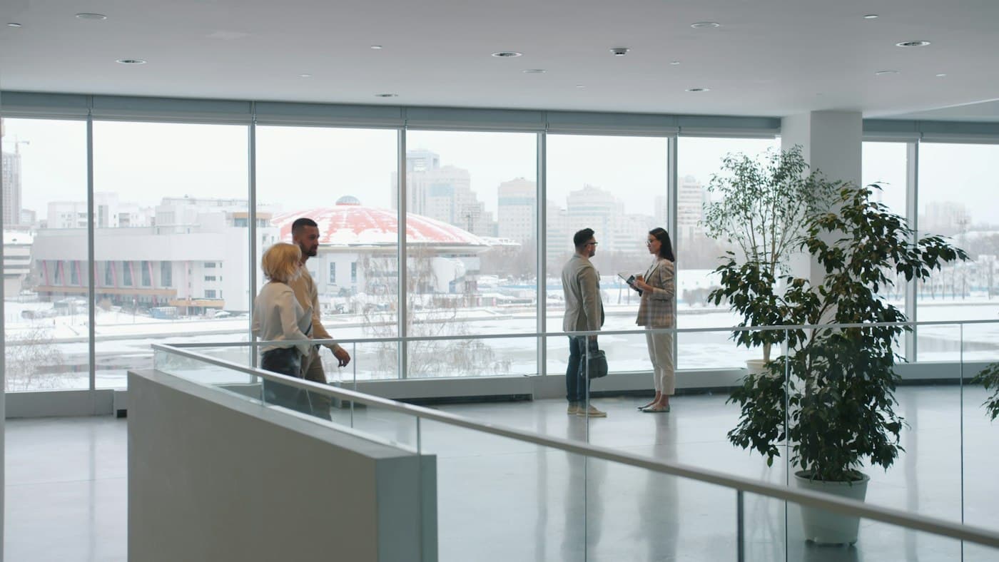 Colleagues talking beside the windows of a bright office lobby.